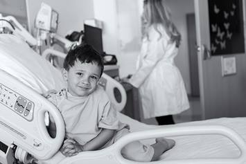 Young boy smiling in hospital bed with physician in background