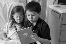 Young girl in hospital bed with older brother reading to her 