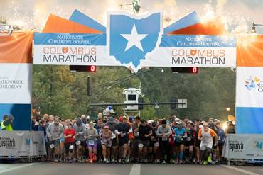 A group of excited marathon participants begin their race at the starting line. Fireworks are on display behind them.