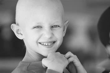 Child with cancer who has lost his hair but is still smiling.