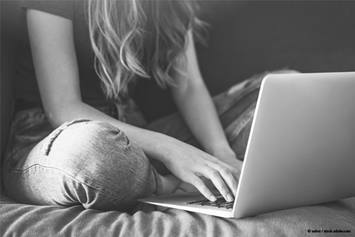 A teenage girl is sitting on a bed with a laptop in front of her.