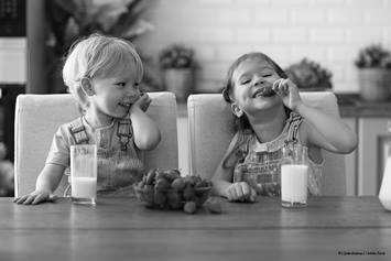 two toddlers eating strawberries and drinking milk.
