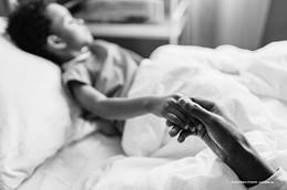 child laying in bed, holding adult's hand