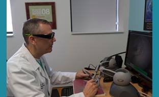 Gregory Wiet is wearing a white coat, seated at a computer with dark glasses on.
