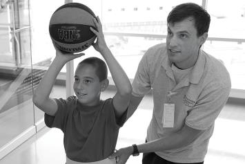 Young rehab patient shooting hoops with a therapist 