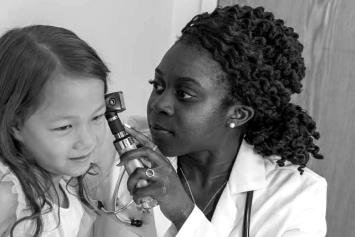 Female resident examining young girl patient's ears