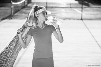 girl holding a tennis racket drinking a bottle of water