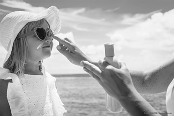young girl with sunglasses and hat receiving help putting on sunscreen